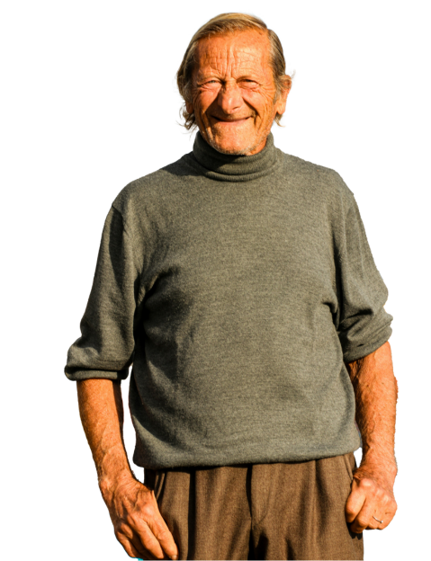 Elderly man wearing a gray turtleneck sweater and brown pants, standing and smiling against a white background.